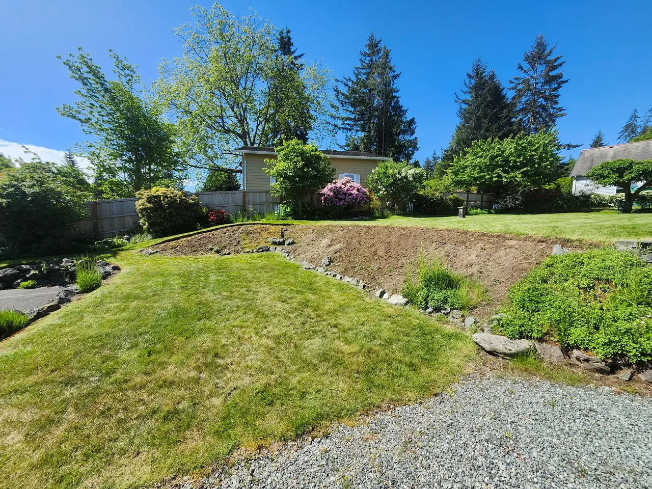 Backyard before — eroded slope with loose rocks, no wall